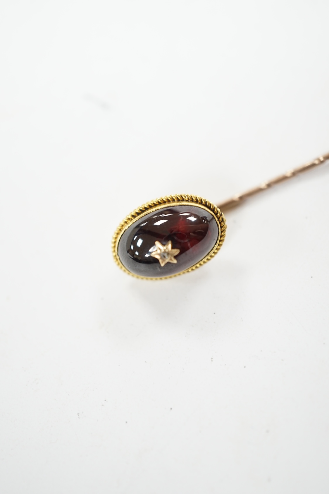 A cased Victorian yellow metal, oval cabochon garnet and diamond chip set stick pin, overall 77mm. Condition - fair